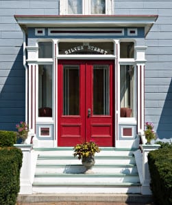 Here is the front door of the silver fountain inn. The door is large and red. There is a potted plant on the stairs of our hotel near dover nh and hedges lead up to the stairs.