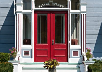 Here is the front door of the silver fountain inn. The door is large and red. There is a potted plant on the stairs of our hotel near dover nh and hedges lead up to the stairs.
