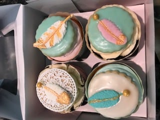 Here are some fun cupcakes gail made at our Durham NH hotel. There are four cupcakes, each with a frosting feather shape on the top. Color scheme is blue, pink, white, and gold.