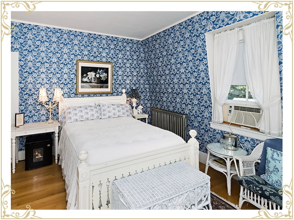 Check out this room at our Durham NH area hotel. This room is called the Eleanor. This is an image of the bed, wicker chairs, white tapestry, and blue victorian wall paper.