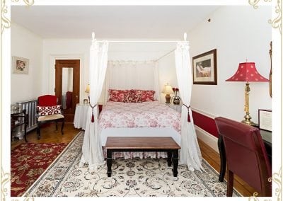 This is the Duchess, one of the room at one of the popular hotels in Dover NH. This image shows a bed and a writing desk. The walls are white with a red trim.